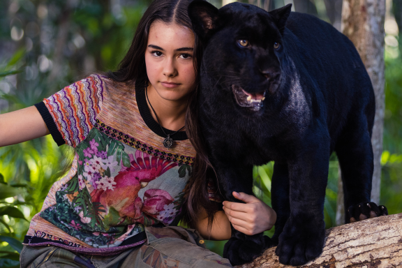 Ella und der schwarze Jaguar auf einem umgefallenen Baumstamm in Wald. © Studio Canal